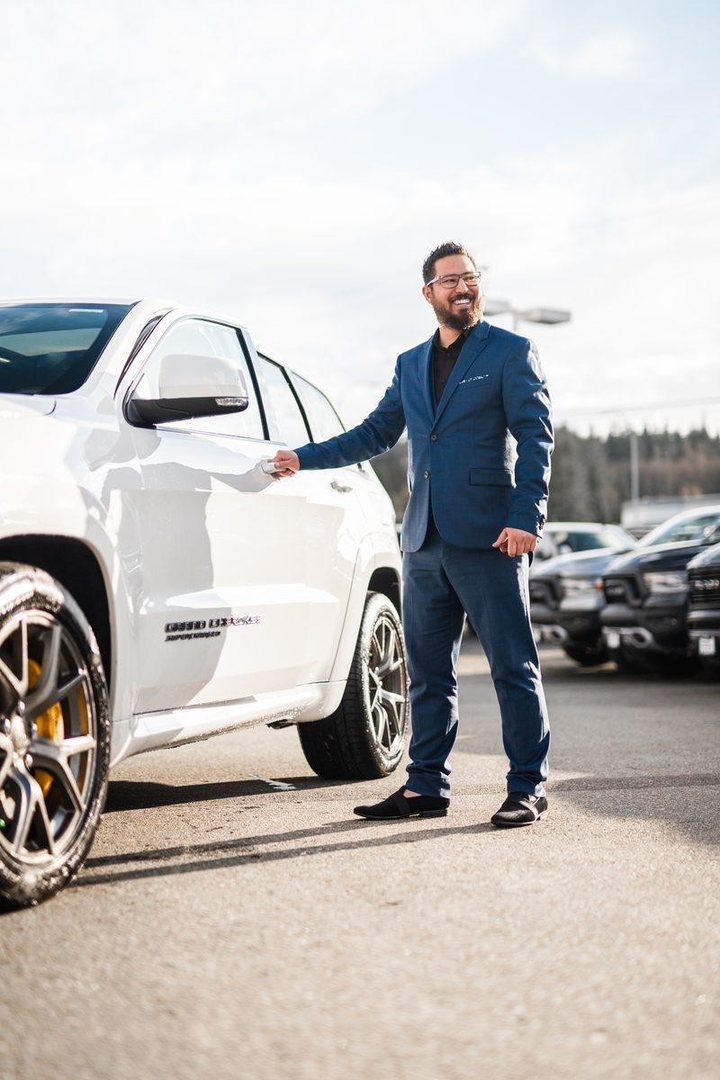 Connor Nishimura, owner of ClearCut Auto Inc., beside a white SUV on a dealer lot